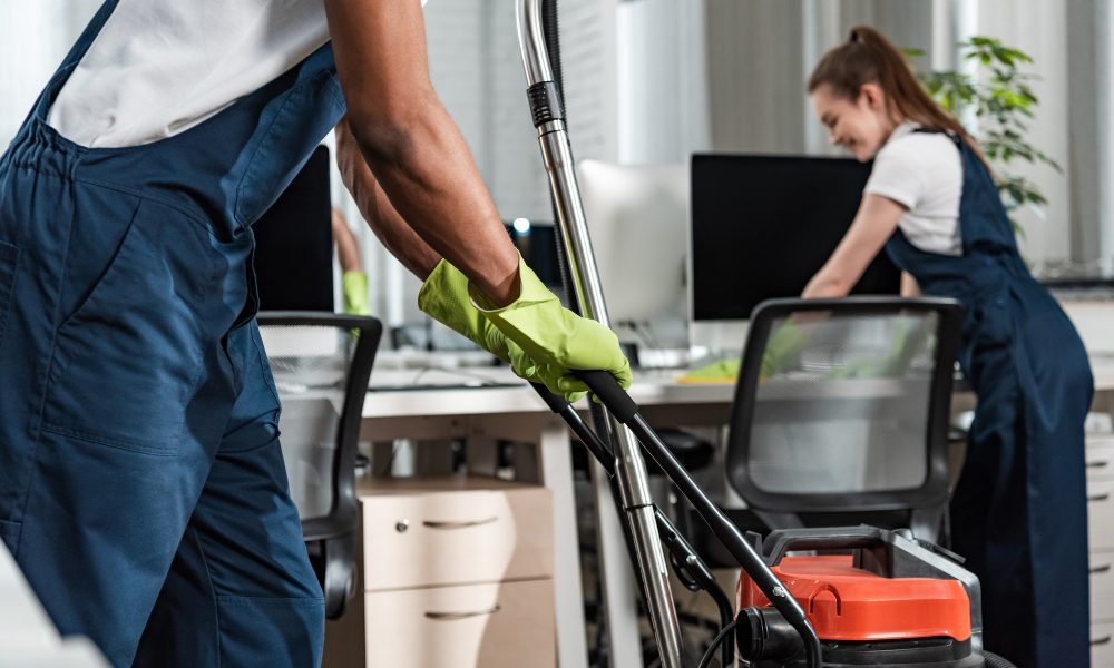 cropped view of african american cleaner moving vacuum cleaner in office