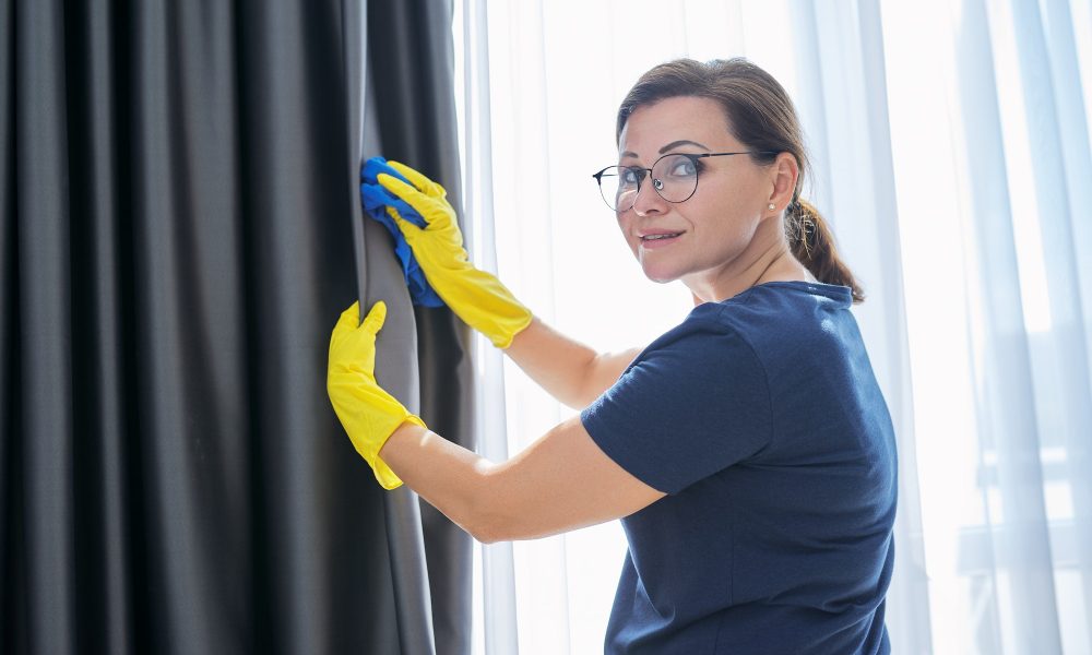 House cleaning, woman in gloves with a rag cleaning curtains