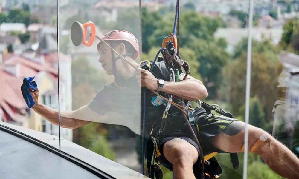 Industrial mountaineering worker cleaning window outside building.