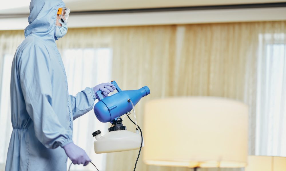 Man in blue protective suit holding disinfectant and standing in the room